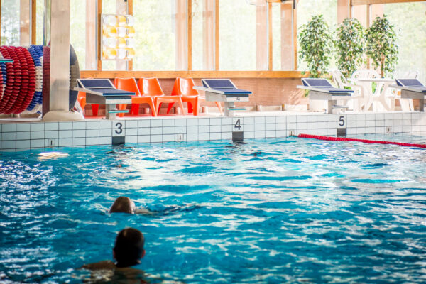 En inomhusbassäng med simmare i vattnet och startpallar längs kanten