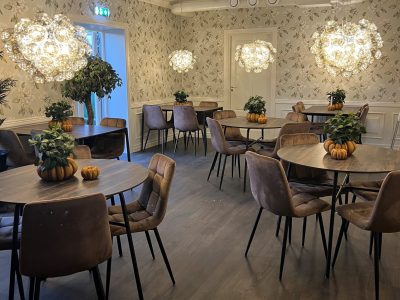En rymlig restaurang eller café med tapetserade väggar, mörkt trägolv, runda bord, mörka stolar och stora, runda ljuskronor, dekorerad med pumpor.
