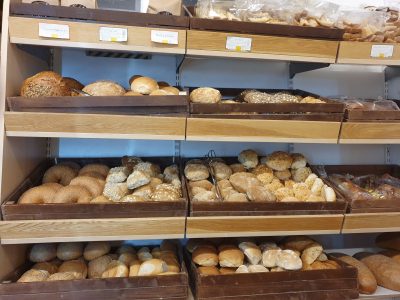 En bagerihylla fylld med olika typer av bröd och bullar i trälådor.