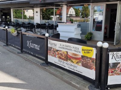 Exteriör av "Kharma Restaurang" i Vimmerby, med uteservering och menyskyltar på staketet.