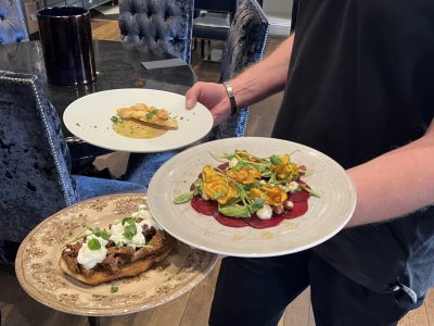 En kypare presenterar tre elegant upplagda förrätter i en restaurangmiljö.