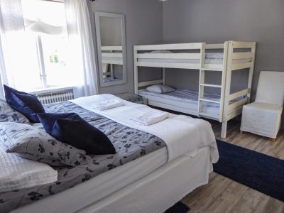 Ett sovrum med en dubbelsäng, en våningssäng och en spegel. Väggarna är grå och golvet är av trä