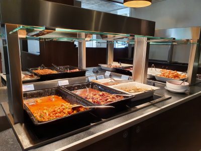 En serveringsdisk med flera kantiner fyllda med olika maträtter, troligen på en buffé, i en modern restaurangmiljö.