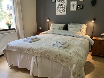 Ett mysigt sovrum i Vimmerby med en stor dubbelsäng, sängbord med lampor, och konst på den mörkgrå väggen. Ett fönster med ljusa gardiner släpper in dagsljus.