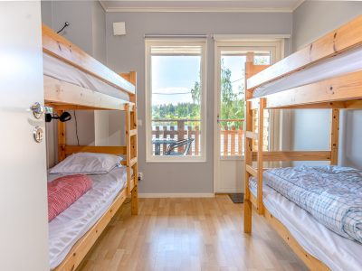 Ett rum med två trä-våningssängar, ett fönster och en balkongdörr som leder ut till en utsikt över ett vattendrag och träd.