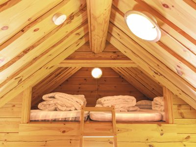 Ett mysigt sovloft med två bäddar och ett ljust träinteriör, syns från en stege nedanför.