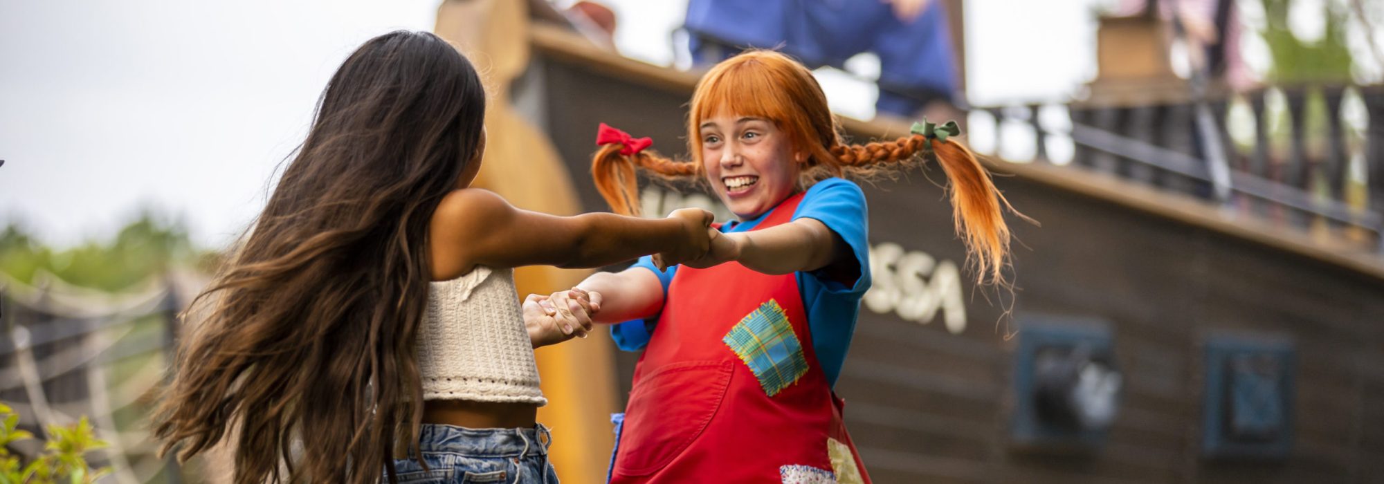 Pippi Långstrump med orange hår och två flätor, dansar hand i hand med en flicka med långt brunt hår.