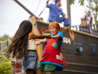 Pippi Långstrump med orange hår och två flätor, dansar hand i hand med en flicka med långt brunt hår.
