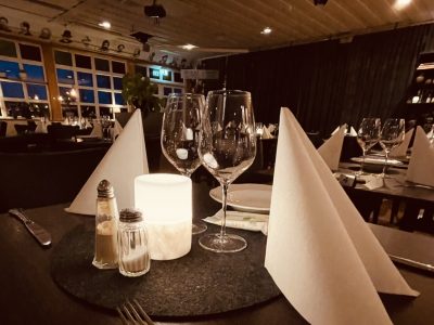 Ett elegant dukat bord med vinglas, vita servetter och en ljuslykta i en dämpad restaurangmiljö.