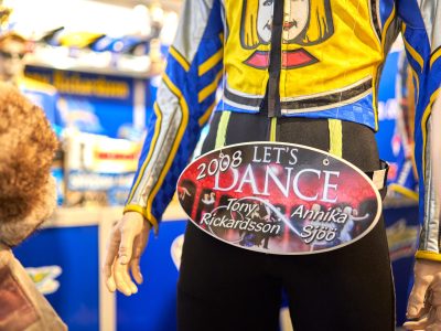 En detaljbild av en gul och blå racingdräkt med ett "Let's Dance 2008"-skylt med namnen "Tony Rickardsson" och "Annika Sjöö". Dräkten visas på en skyltdocka.
