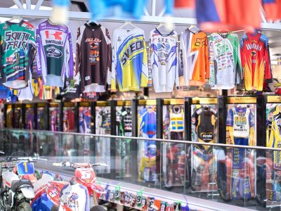 Ett museum fyllt med motorsportmemorabilia. Ett stort antal färgglada racingtröjor hänger från taket, medan racingdräkter visas i montrar under ett glasräcke. På bottenvåningen syns också motorcyklar och nummerplåtar.