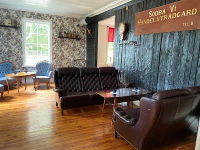 En mysig lounge med lädersoffor, fåtöljer, trägolv och en vägg med en skylt för "Södra Vi Handelsträdgård.