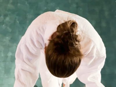 Bilden visar en person i vit badrock som kliver ner i en blå pool.