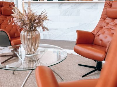 En lobby med bruna läderfåtöljer och ett glasbord med torkade blommor. I bakgrunden syns en reception med en person bakom disken.