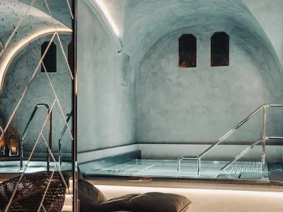 En stilren inomhuspool i Vimmerby med ljusgrå, minimalistisk design, välvda tak och silverfärgade räcken, med en jacuzzi i bakgrunden och dekorativ spegelverk.