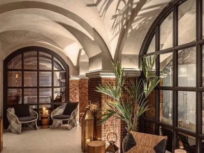 En lounge i Vimmerby med elegant välvt tak, stora välvda fönster, och mysiga sittplatser. Rummet är inrett med rottingmöbler, växter, lyktor och tegelmönstrade väggar.