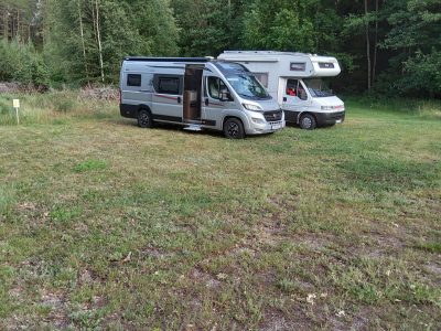 Två husbilar står parkerade på en gräsbevuxen yta omgiven av skog.